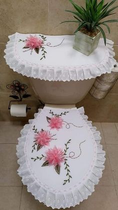 a white toilet with pink flowers painted on the lid and under it, next to a potted plant