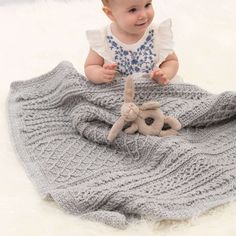 a baby sitting on top of a blanket holding a stuffed animal