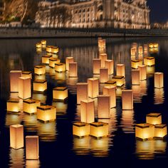 many lit up cubes floating in the water with buildings in the background at night