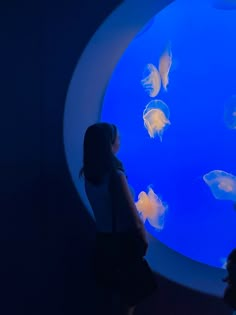 two people looking at jellyfish in an aquarium tank with blue lights on the wall