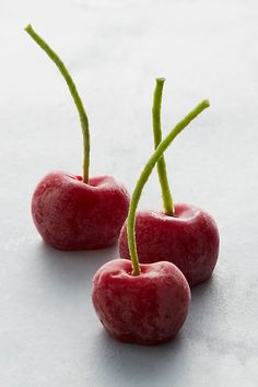 two cherries with green stems on a white surface