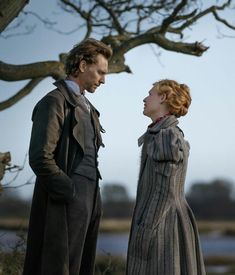 a man and woman standing next to each other in front of a tree with no leaves