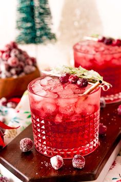 two glasses filled with cranberry punch on top of a wooden table next to christmas decorations