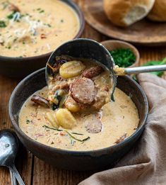 two bowls filled with soup on top of a wooden table next to bread and spoons