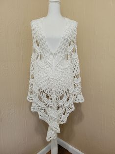 a white crocheted shawl on a mannequin head stand in front of a wall