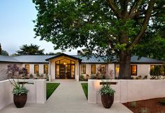 a white house with two large planters in front of it and a tree on the other side