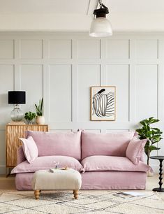 a living room with a pink couch and ottoman next to a wall mounted art piece