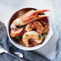 a bowl filled with shrimp and vegetables on top of a table next to a spoon