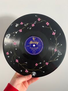 a person holding up a black plate with pink flowers on it and the words merry written in blue