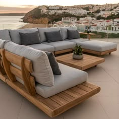 a couch and table sitting on top of a patio next to the ocean with buildings in the background