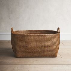 a large woven basket sitting on top of a wooden floor next to a white wall