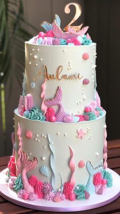 a three tiered cake decorated with pink, blue and green under the sea theme