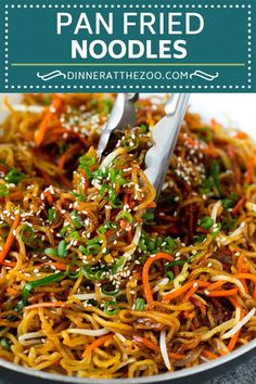 a pan fried noodle dish with carrots and green onions in it, topped with sesame seeds