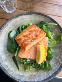 two pieces of salmon on top of broccoli and spinach in a bowl