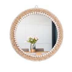 a round mirror hanging on the wall above a wooden table with flowers in a vase