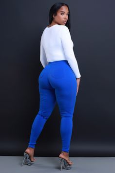 a woman in blue pants and heels is posing for the camera with her hands on her hips