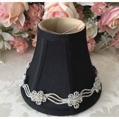 a black lamp shade with crystal beading on the top and bottom, in front of pink flowers