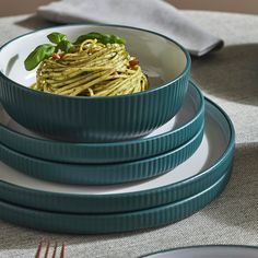 three plates with pasta and spinach on them sitting on a table next to silverware