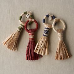 three tasselled keychains are shown on a white tablecloth, one is red and the other is beige