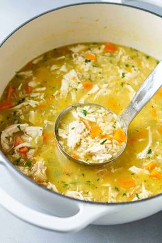 a ladle full of chicken and rice soup in a white pot with a spoon