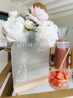 a table topped with flowers and drinks on top of a wooden table next to a vase filled with watermelon