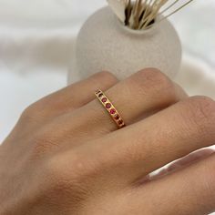 a woman's hand with a gold ring on it and a vase in the background