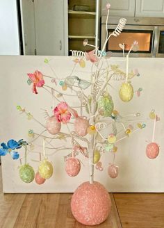 a tree with ornaments hanging from it's branches on a wooden table in front of a refrigerator