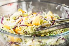 a salad in a glass bowl with two serving utensils