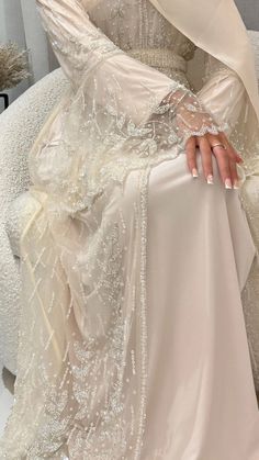 a woman sitting on top of a white couch wearing a dress with long sleeves and beading