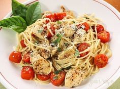 a white plate topped with pasta covered in chicken and cherry tomatoes next to basil leaves