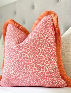 a pink and orange leopard print pillow sitting on top of a white couch next to pillows