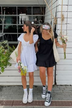 spring and summer outfit ideas for women. girl wearing mini flowy white dress with white high top converse, holding a bouquet of flowers. other girl wearing black mini flowy dress with black high top converse. posing in front of white wall. instagram picture idea Dresses And Converse, Converse Outfit Summer, Natalie Downey, Outfits Primavera Verano, White Converse Outfits, Dress With Converse, Sundress Outfit, Outfits Primavera, Looks Pinterest