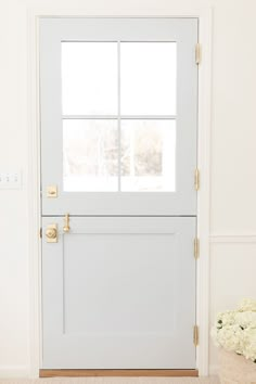 a white front door with two windows and a basket full of flowers on the floor