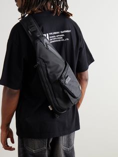 a man with dreadlocks wearing a black t - shirt and carrying a messenger bag