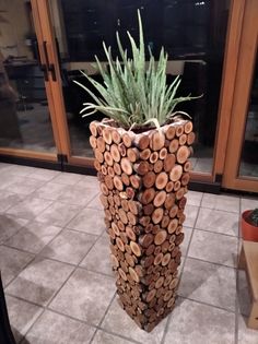 a tall planter made out of logs on the floor in front of a glass door