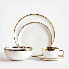 white and gold dinnerware set with matching saucers, cups and plates on a white background