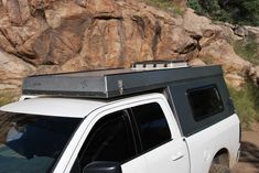 a white pick up truck parked in front of a large rock formation with a roof rack on top