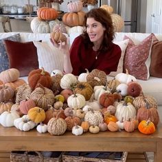 a woman sitting on a couch surrounded by lots of pumpkins and gourds