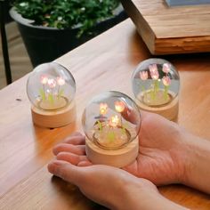 two clear glass vases filled with flowers on top of a wooden table next to a person's hand