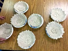 five white bowls sitting on top of a wooden table next to a person's hand