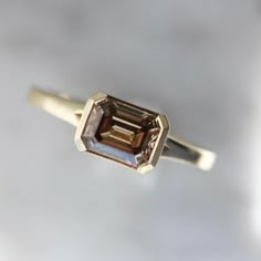 Why I Love It: Nothing sour about this amaretto! Fall in love with this statement ring that features a 1.22 carat deep champagne emerald cut diamond. Set east-west with a unique half bezel, and a shank with a small split prong. Finished in 14k Yellow Gold, this ring is stackable. Read more about the collection in this blog post. The Details: 14k Yellow Gold 1.22 Carat Champagne Emerald Cut Diamond GIA Graded Diamond VS1 Clarity Fancy Dark Orangey Brown (Color Grade) Band Width Measures Approx. 1