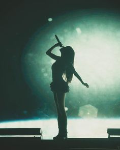 a woman standing on top of a stage holding a microphone in her hand and looking at the sky