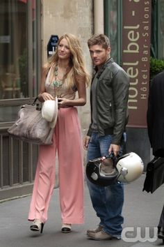 a man and woman walking down the street with helmets on their heads, carrying bags