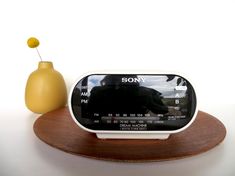 an alarm clock sitting on top of a wooden stand next to a vase with a yellow flower in it