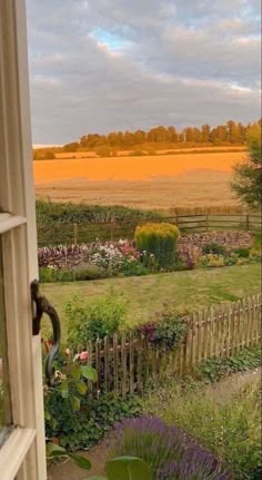 an open window looking out at a field and trees in the distance, with a wooden fence