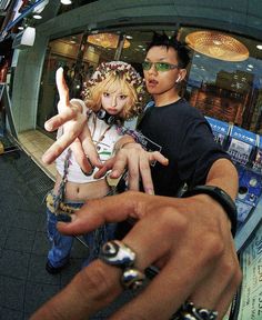 two people standing in front of a store holding their hands up and pointing at the camera