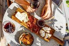 two people sitting at a table with wine and cheeses on it, holding glasses of wine