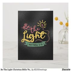 a card with the words be the light on it next to a vase filled with flowers