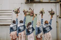 four women are holding flowers in front of a building with their hands up to the sky