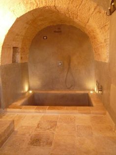 a bathroom with stone walls and an oval bathtub in the center, surrounded by tile flooring